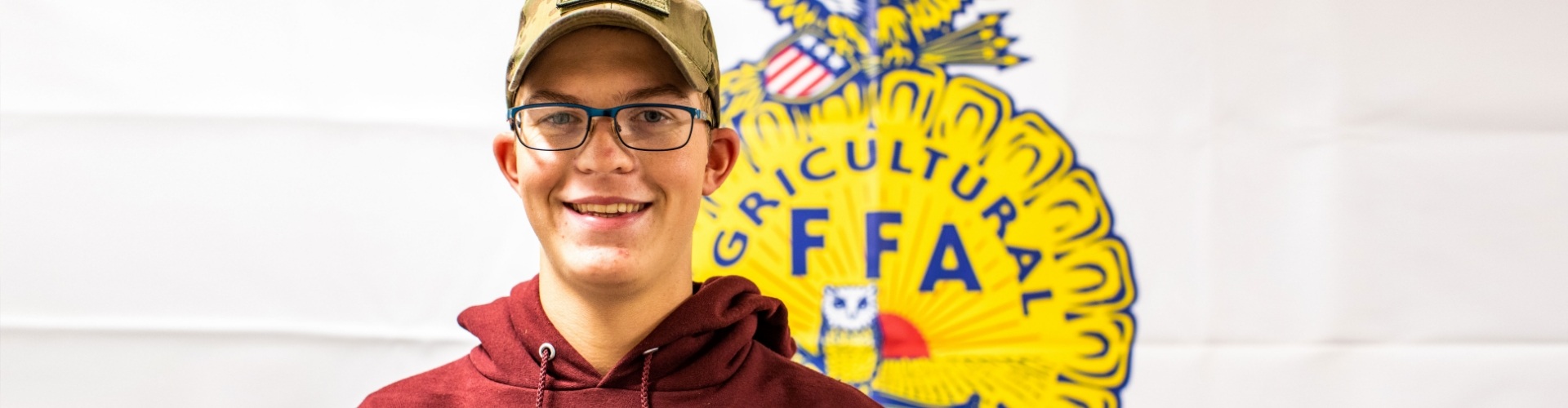 FFA student standing in front of the FFA Logo on a wall