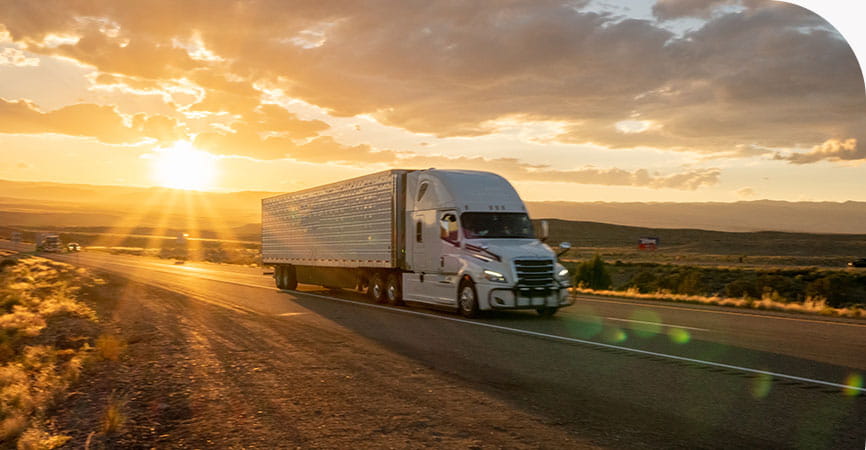 Semi truck driving down a rural road in the sunset