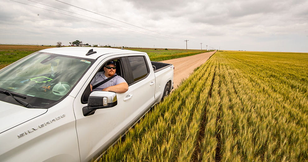 Man in white truck driving beside a field