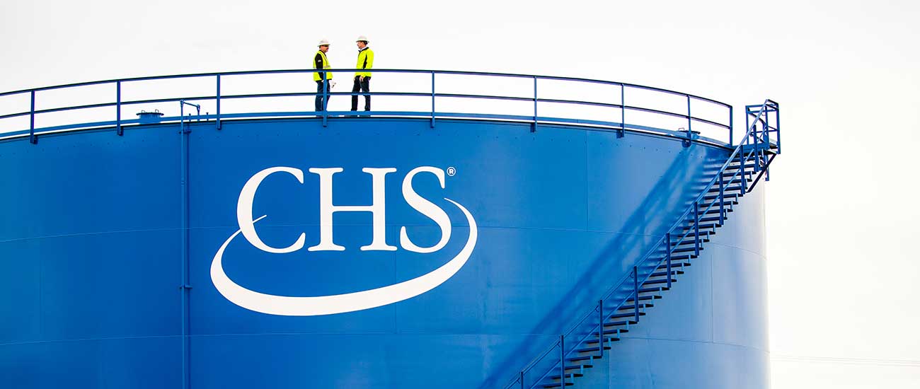 two workers on top of large bulk tank with CHS logo