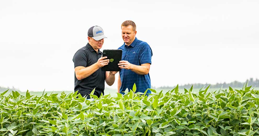 two men in field looking at tablet