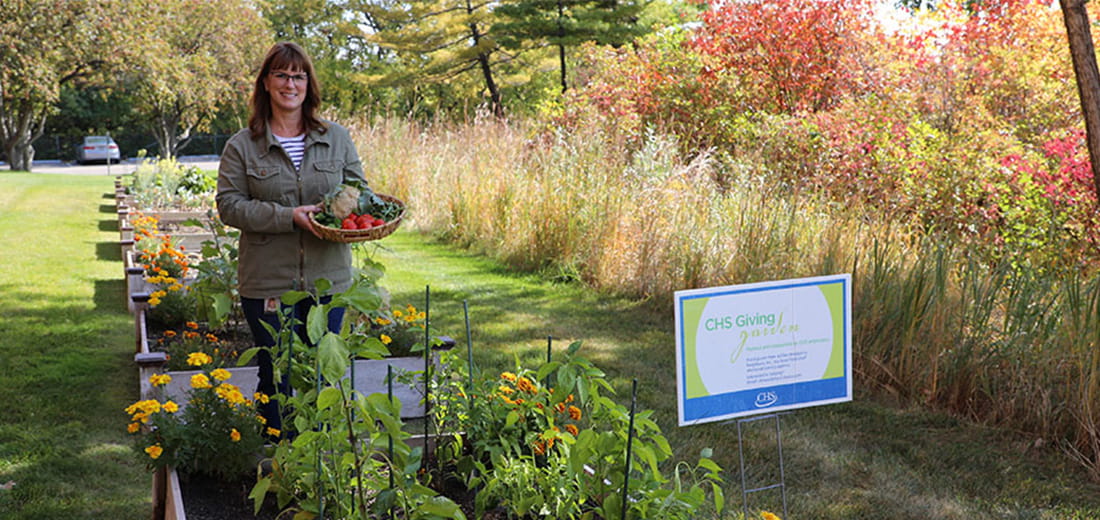 Danielle Fischer standing with a basket of vegetables beside the CHS Giving Garden