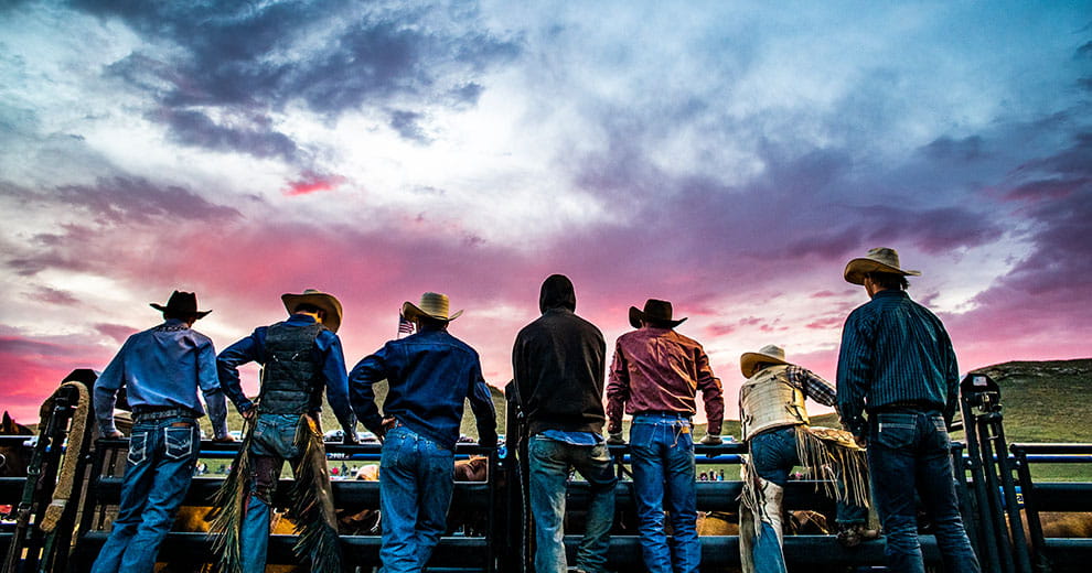 Cowboys lined up along a fence during sunset at rodeo