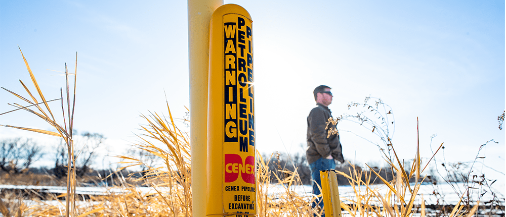 Farmer walking next to a buried pipeline warning post