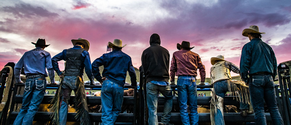Cowboys line up along a fence with the sunset.