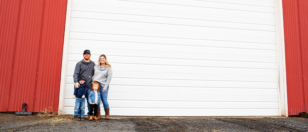 The Jones family stands in front of a red machine shed with a white overhead door.