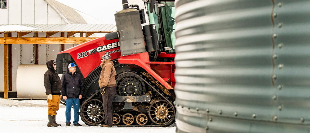 Art and Joe Ridl stand next to their large red tractor while talking with a Cenex certified energy specialist.