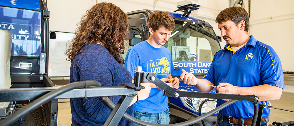 A teacher talks to students in front of farm machinery at South Dakota State University.