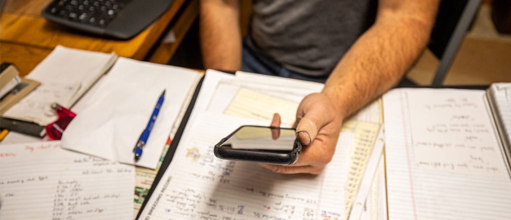 A phone is held at a desk filled with papers.