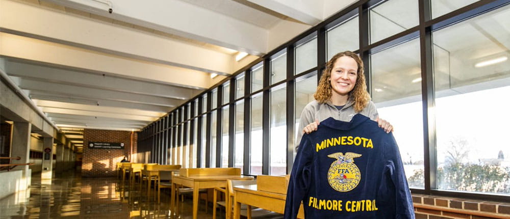 College student sitting on a desk holding her FFA jacket.