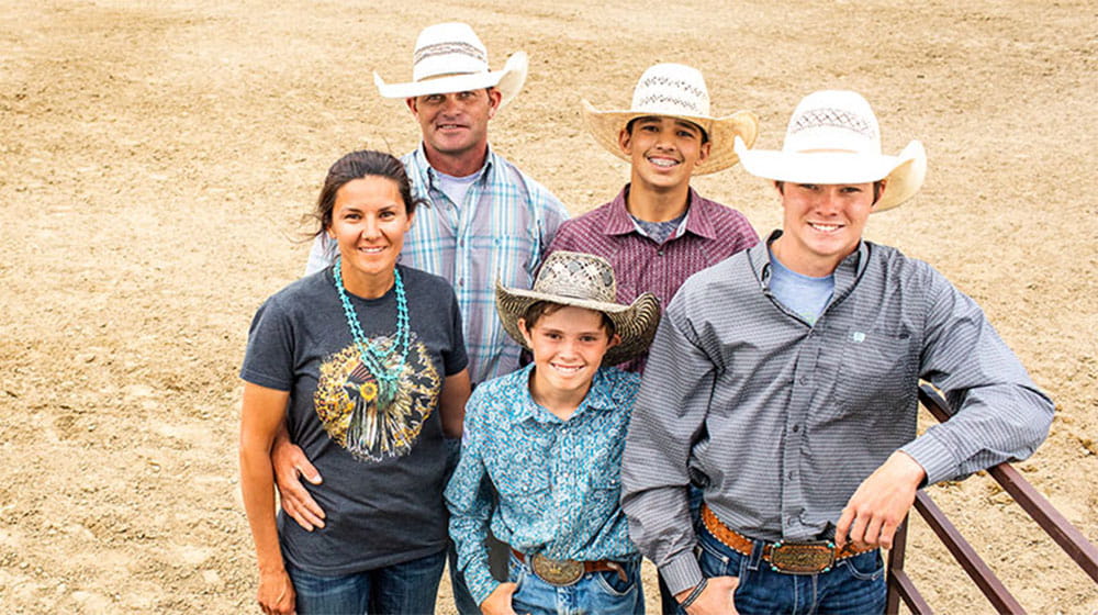 Family poses on the rodeo grounds, wearing cowboy hats and jeans