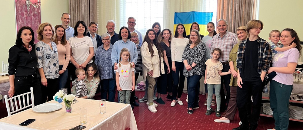 Group of people posing in hotel dining area with flag of Ukraine pinned to the curtains behind them